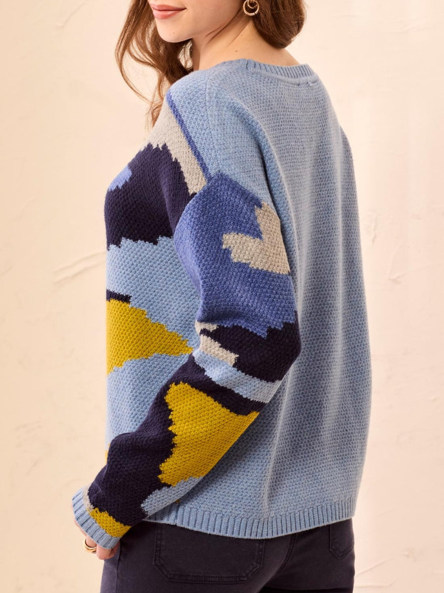 Light blue knit sweater with abstract color block pattern in yellow, navy, and cream on the sleeve and front panel.