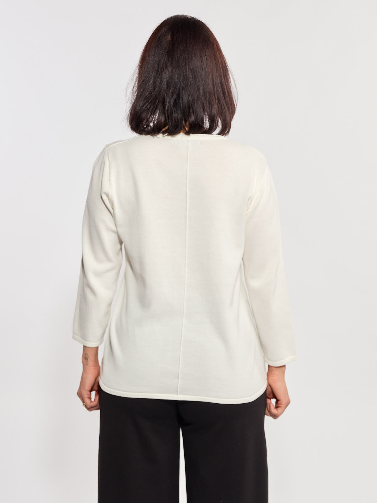 Back view of a white long-sleeve sweater paired with black loose pants against a plain background.