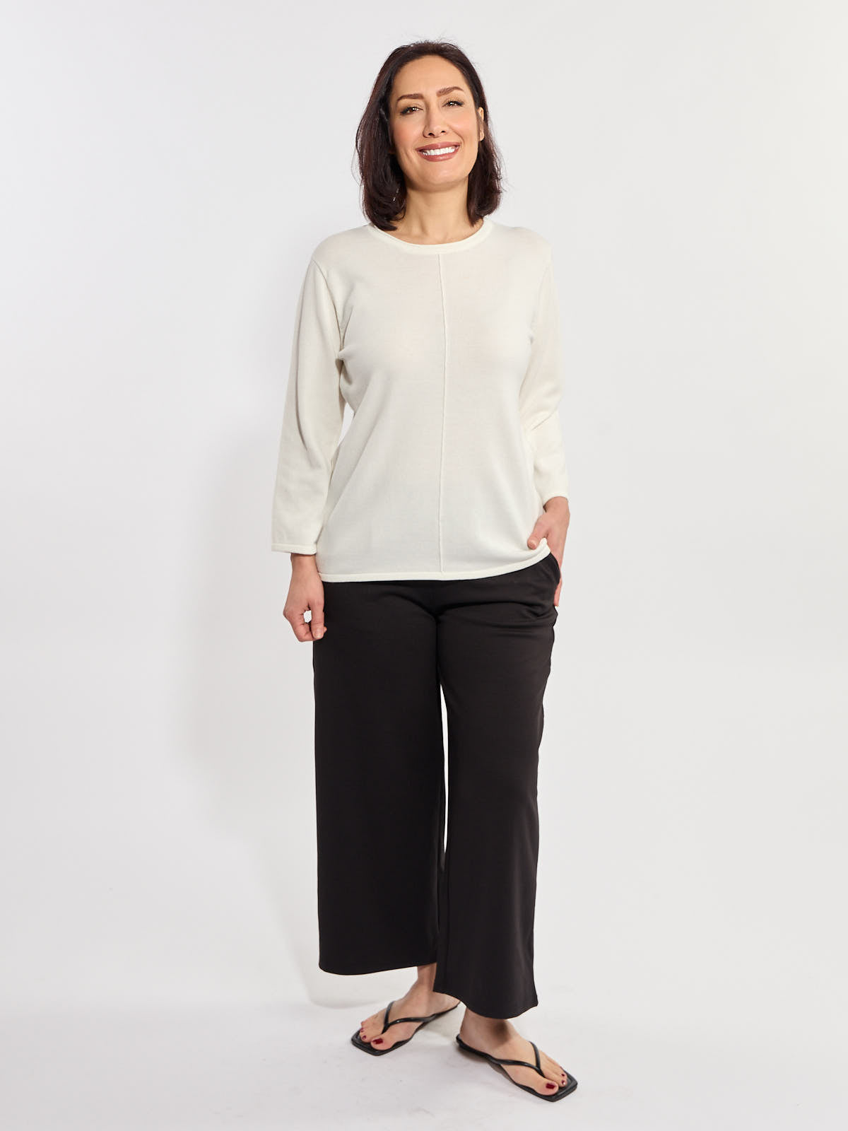 Smiling figure in a cream long-sleeve top paired with loose black wide-leg pants and black flip-flops.