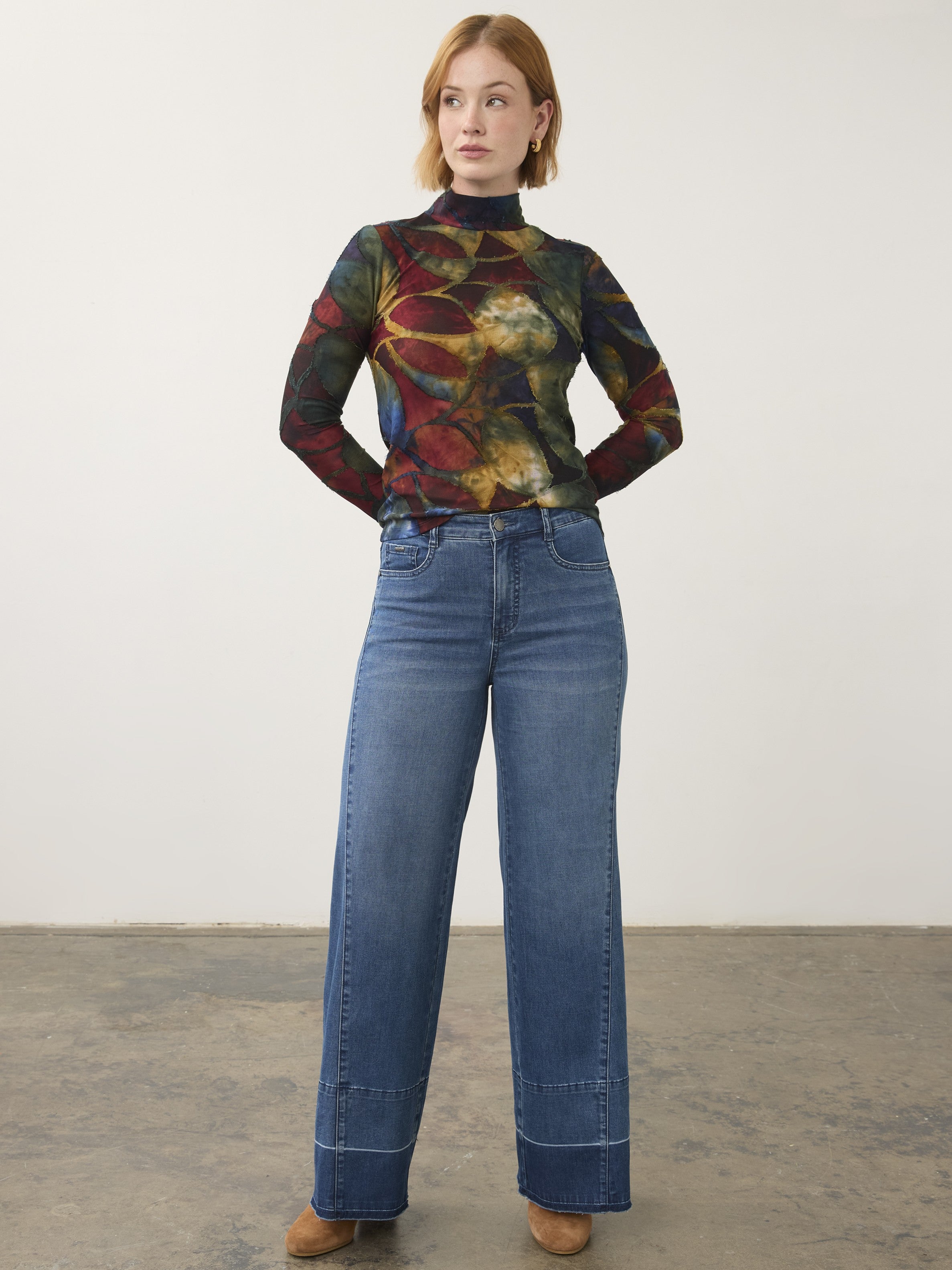 Multicolored long-sleeve top paired with high-waisted wide-leg blue denim jeans and brown shoes on a plain background.