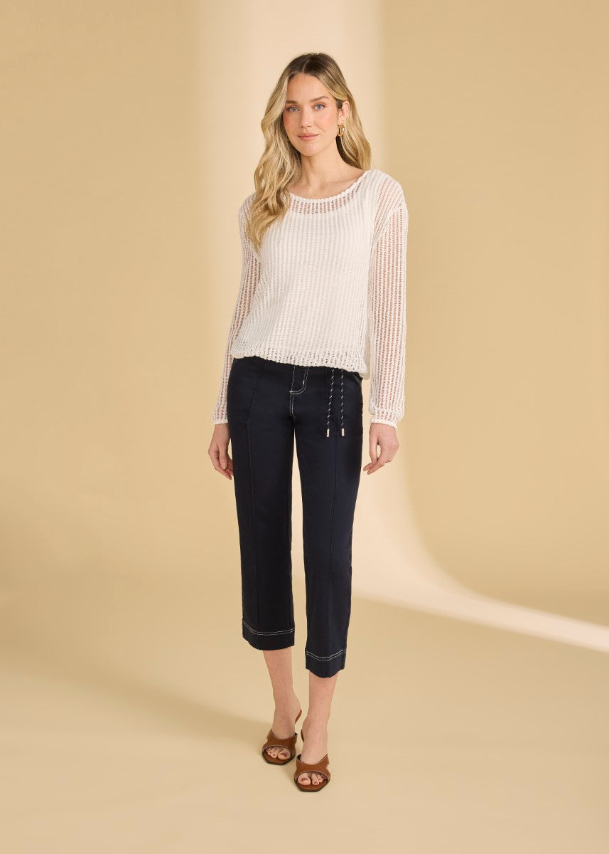 Person wearing a white long-sleeve ribbed top with navy cropped pants and brown open-toe heels against beige background
