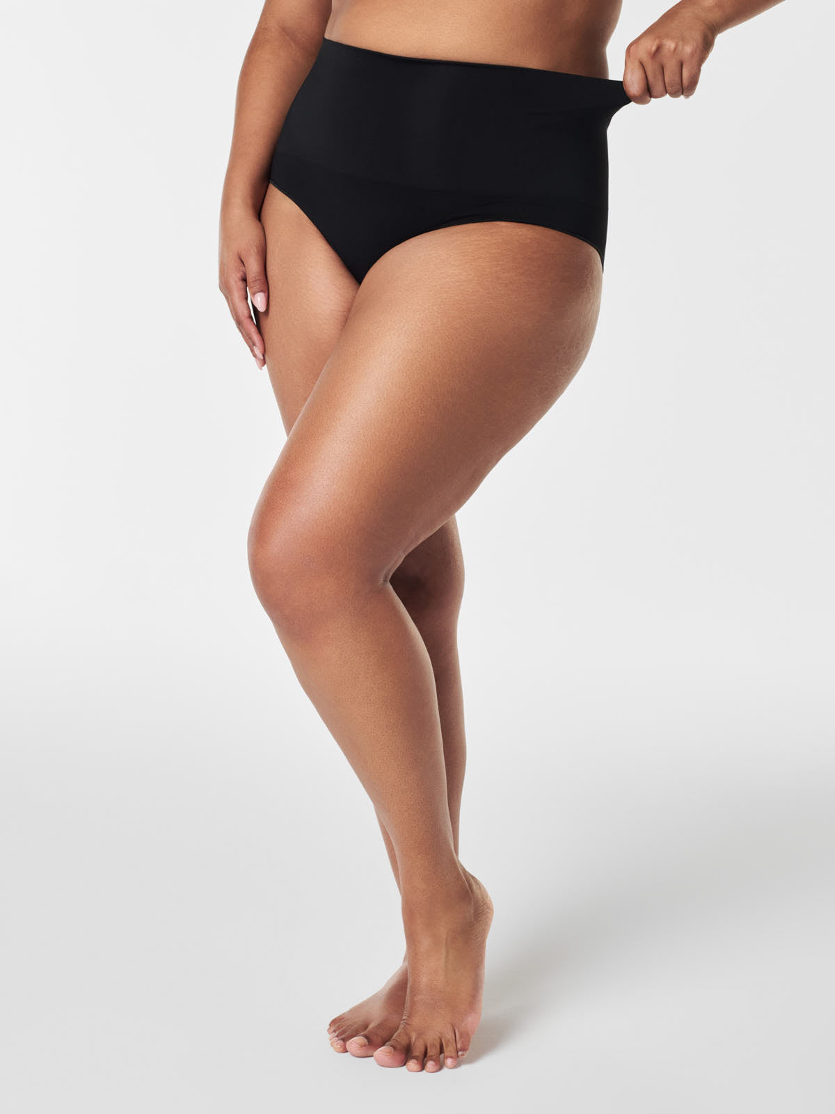 Close-up of a person adjusting black SPANX EcoCare Seamless Brief by Spanx, highlighting fit and smooth design.