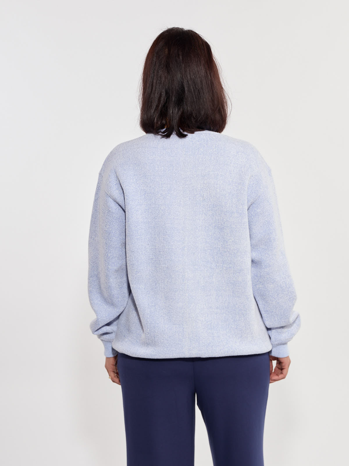 Light blue textured sweater with long sleeves paired with dark blue pants against a plain background.