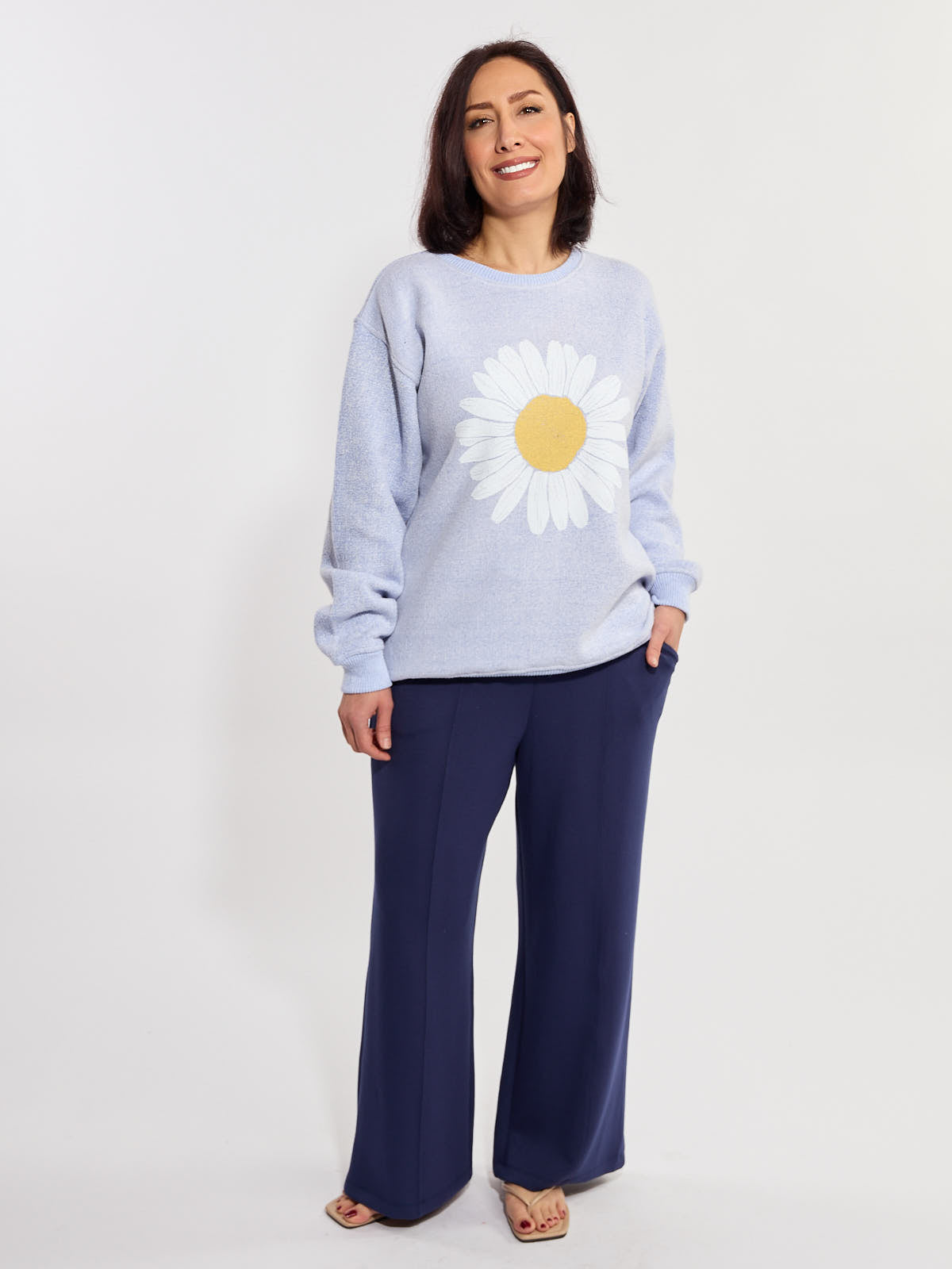 Light blue sweater with a large white and yellow daisy graphic paired with navy wide-leg pants and sandals.