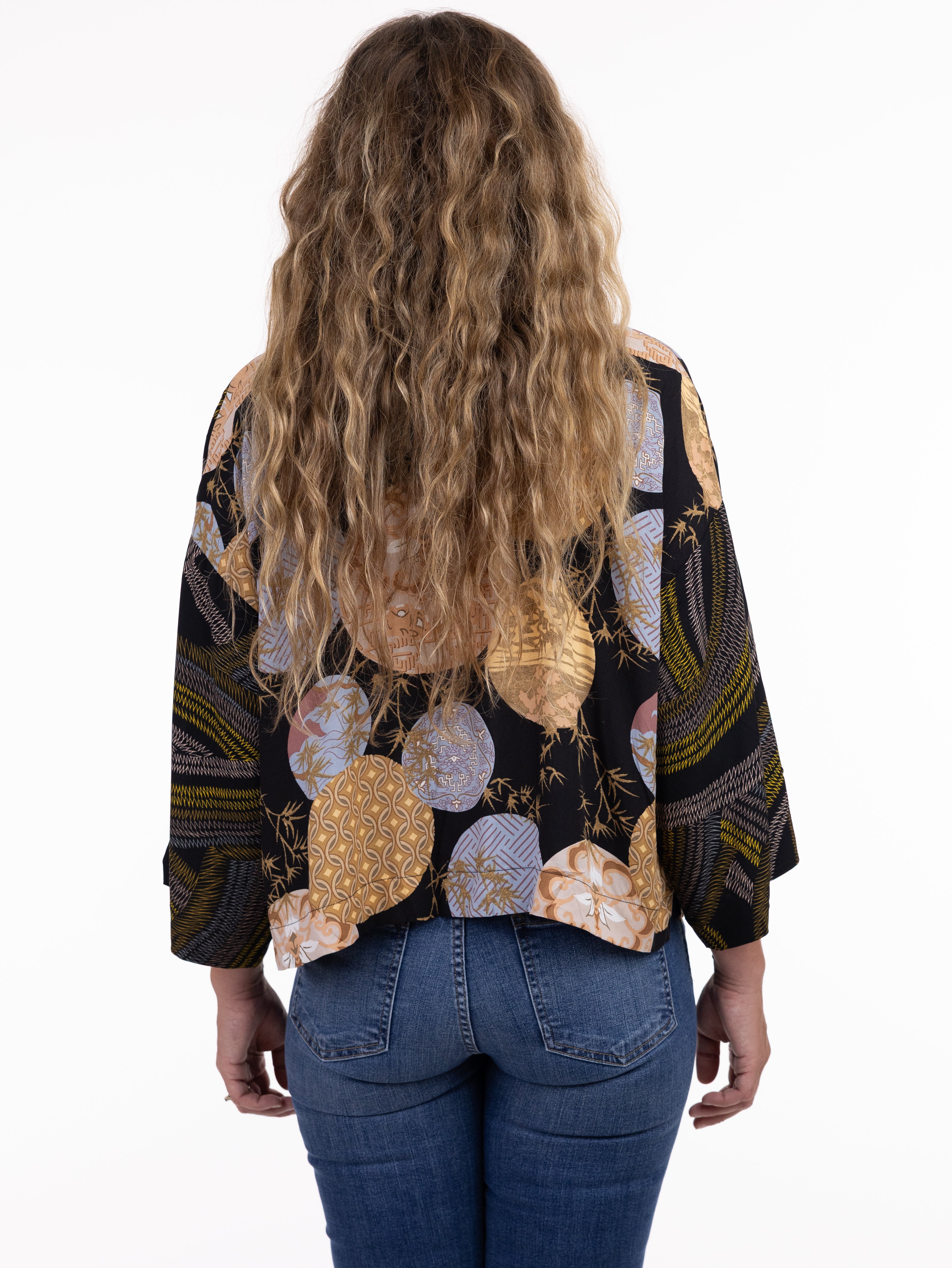 Black patterned long sleeve top paired with blue denim jeans shown from the back with wavy hair visible