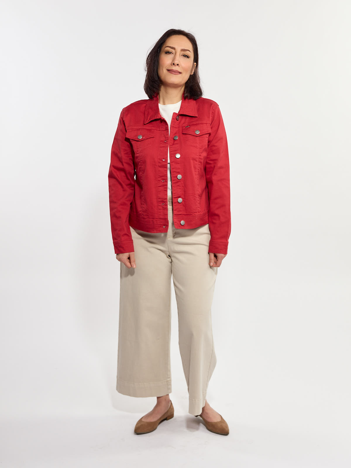 Red denim jacket with button front and chest pockets paired with wide beige pants and brown flats on light background