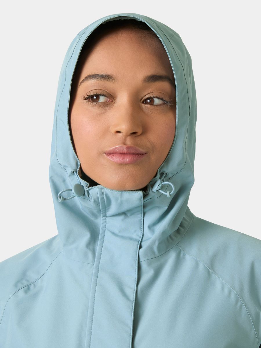 Close-up of a face partially covered by a light blue hooded jacket with drawstrings on a neutral background.