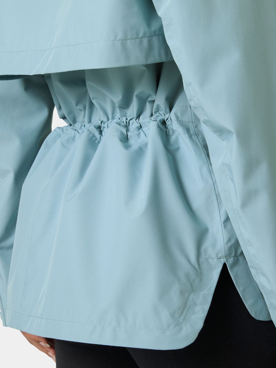 Light blue outerwear jacket with gathered elastic waistband and side slit detail over dark pants.