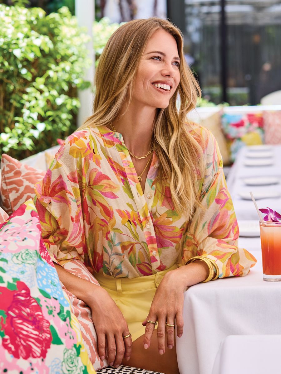 Smiling model in colorful setting wearing Tribal Late Bloom Muted Floral Dolman Sleeve Top by Tribal Sportswear Inc.