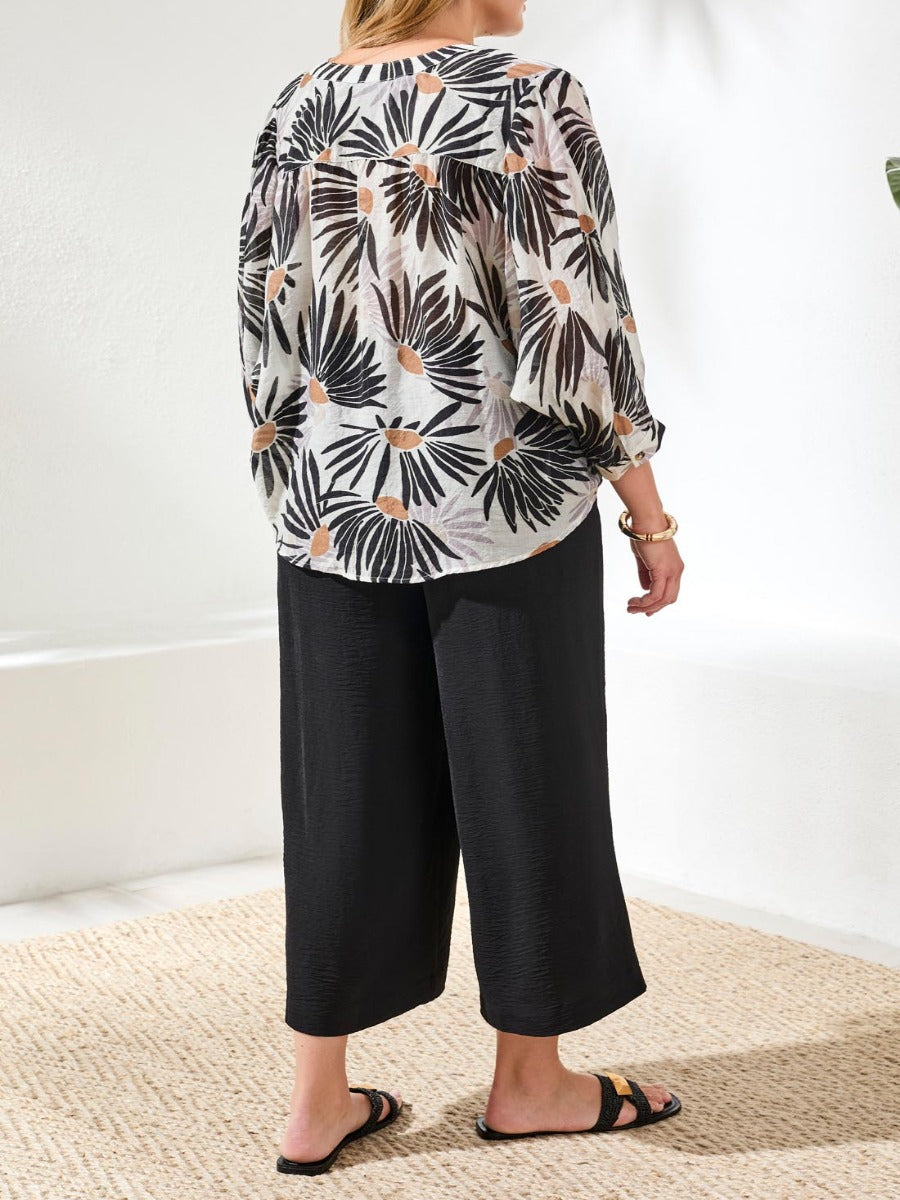 Back view of Tribal Late Bloom Muted Floral Dolman Sleeve Top by Tribal Sportswear Inc. with black pants and sandals