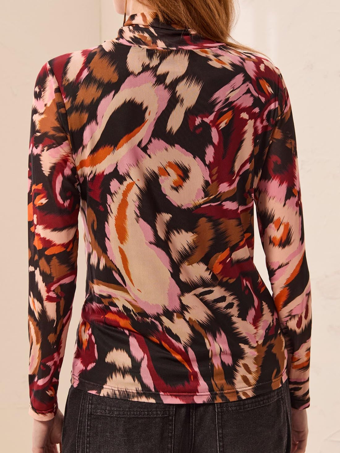 Abstract patterned long-sleeve top with swirls in shades of pink, brown, red, and beige viewed from the back