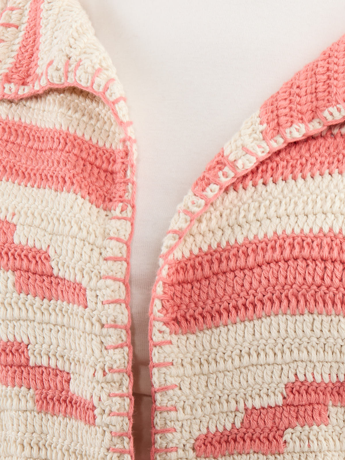 Close-up of a cream and pink crochet sweater with textured stripes and detailed stitching along the edges