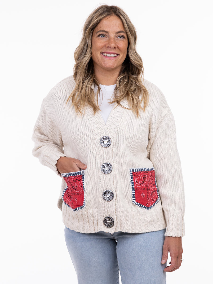 Cream knit cardigan with large buttons and red patterned patch pockets worn over a white top and light jeans