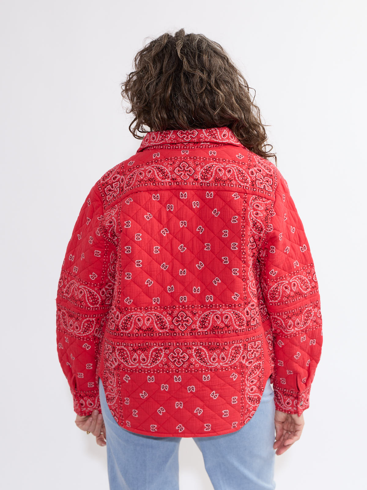 Back view of a red Shannon Passero Bandana Quilted Shacket with paisley pattern from SHANNON PASSERO INC worn with light blue jeans.