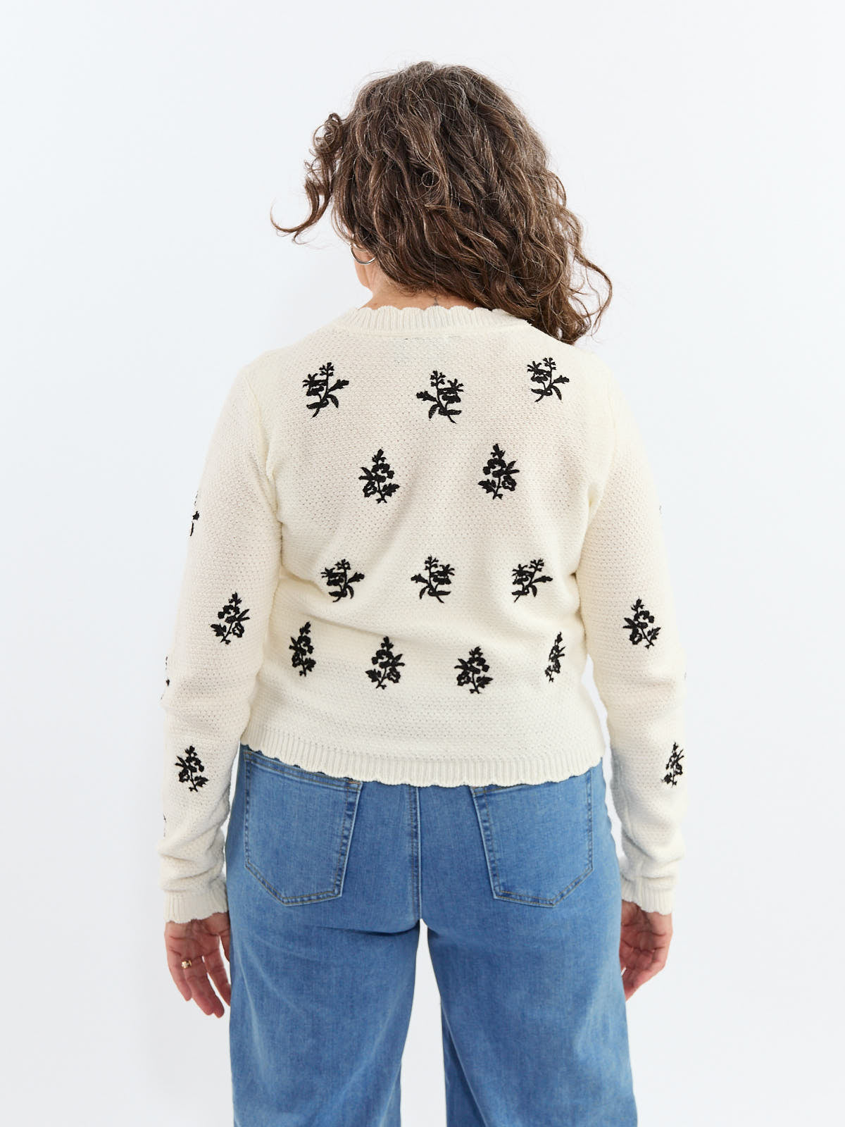 Ivory knit sweater with black floral embroidery, worn with blue denim jeans, shown from the back