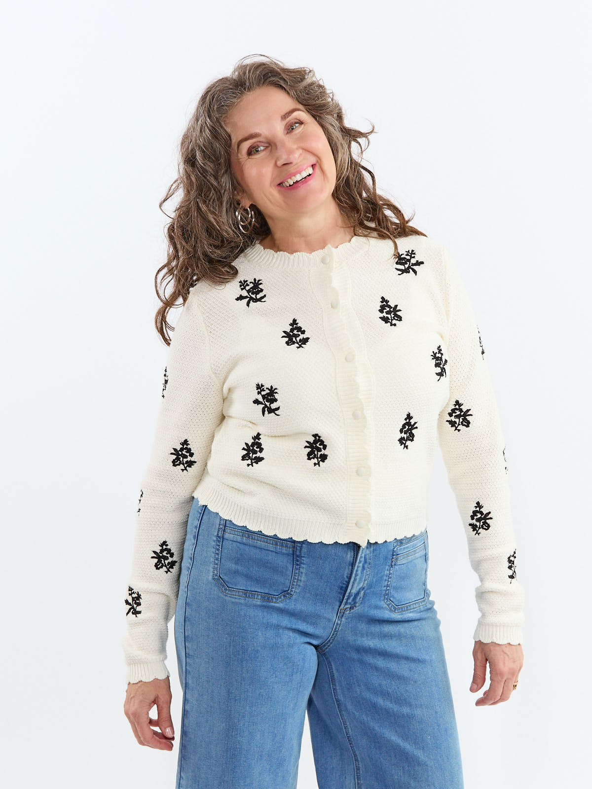 Smiling model wearing Razzle Dazzle Embroidered Flower Button Crew Cardigan in ivory with black floral accents