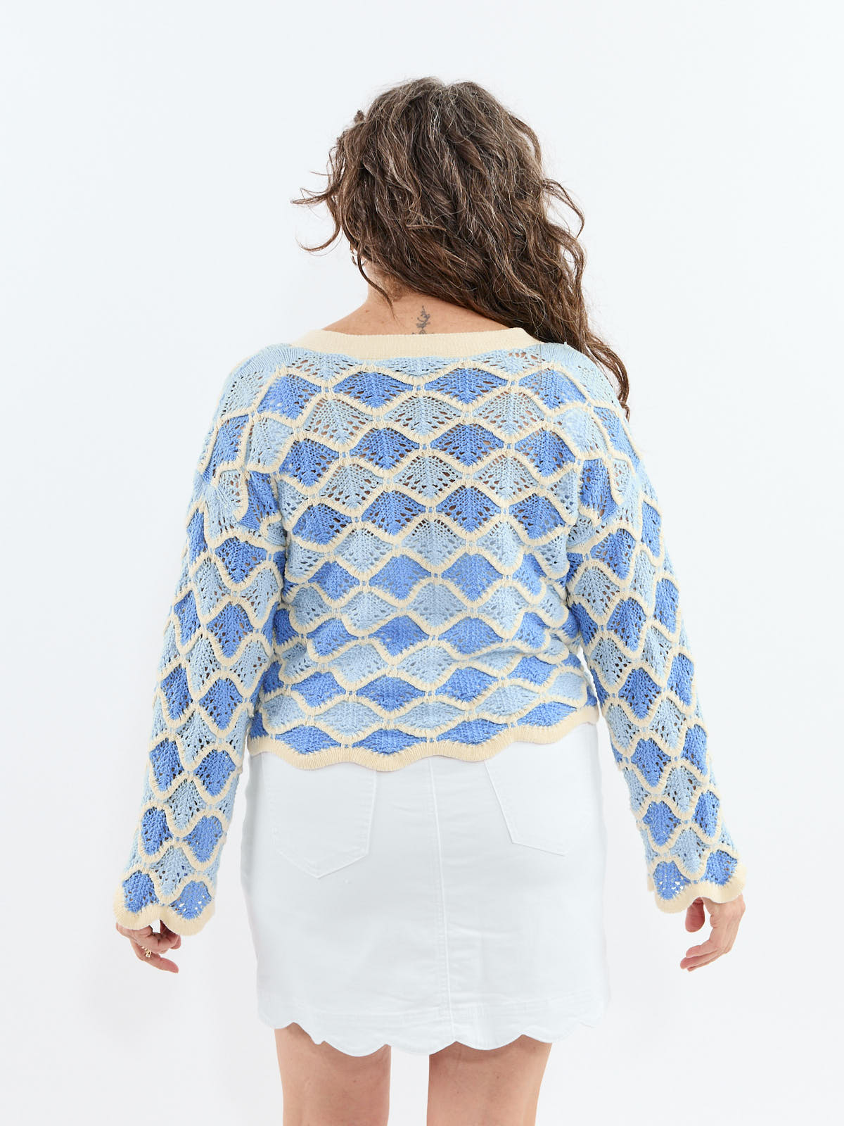 Loose knit blue and cream sweater with a diamond pattern paired with a white scalloped-edge skirt viewed from behind.