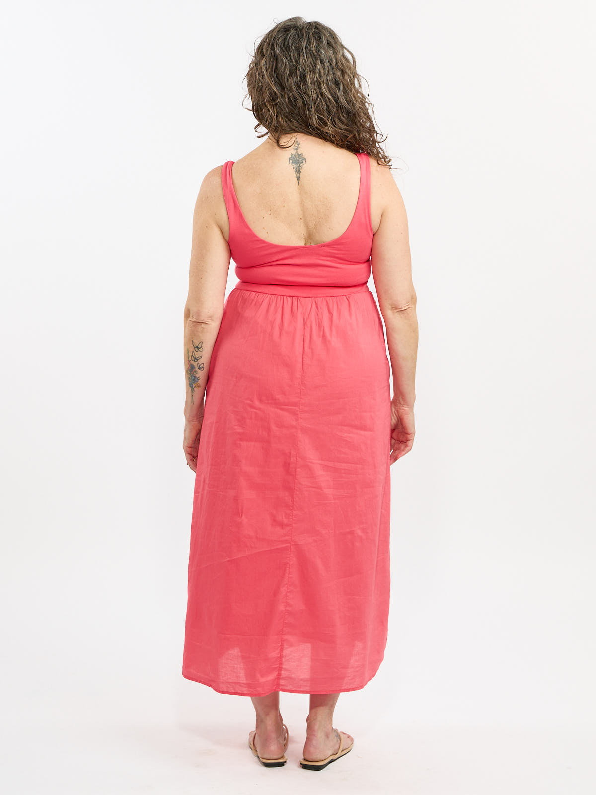 Back view of a sleeveless coral dress with a low scoop back and calf-length hem on a light background.