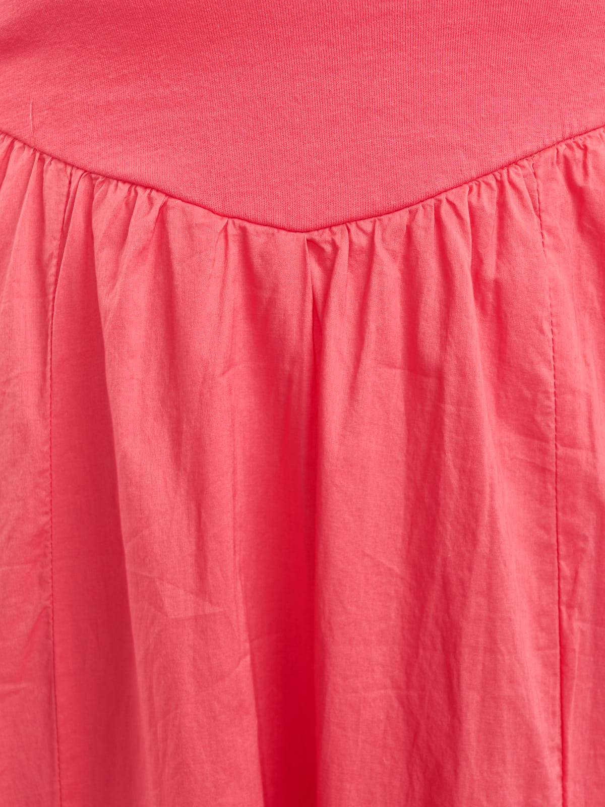 Close-up of coral pink fabric detail with gathered seam and smooth texture on a garment.