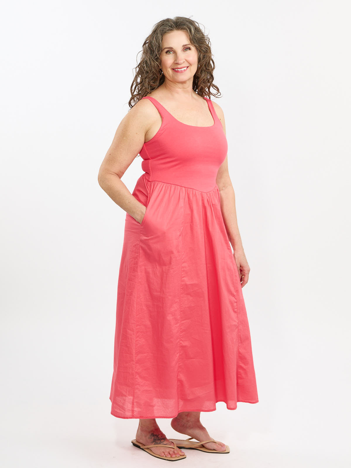 Coral sleeveless long dress with side pockets and a square neckline displayed on a model against white background.