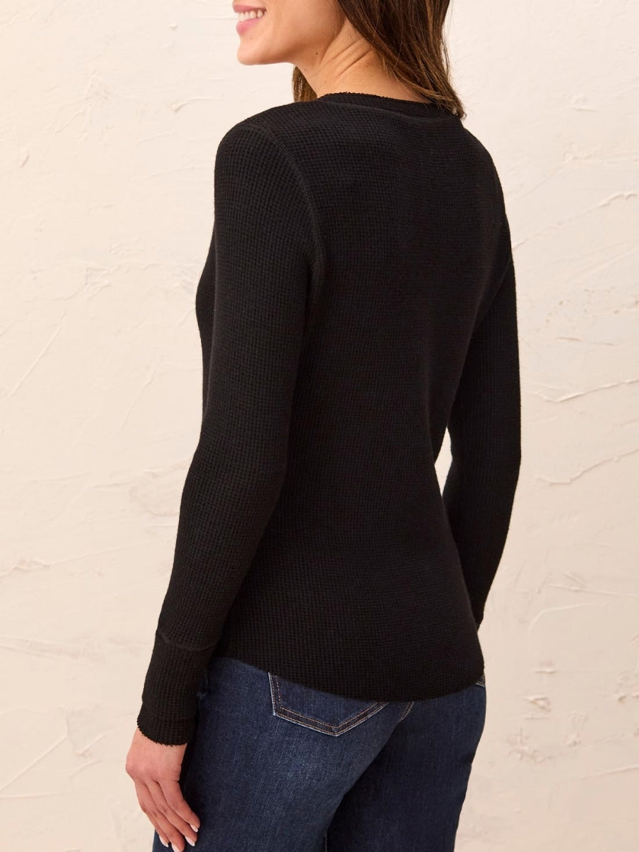 Long-sleeve black textured sweater paired with dark blue denim jeans against a neutral wall background.