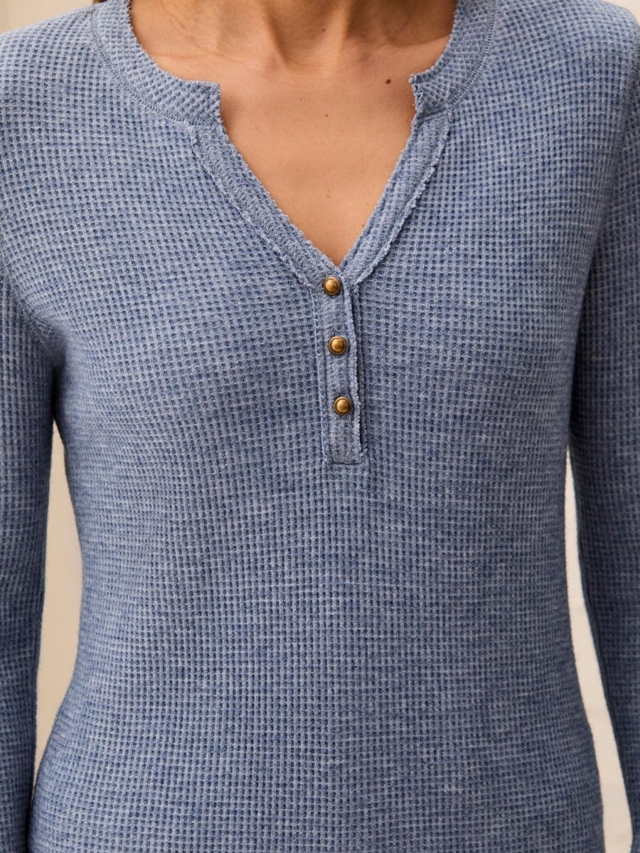 Close-up of a blue textured long-sleeve top with a notch neckline and three brass buttons down the front.