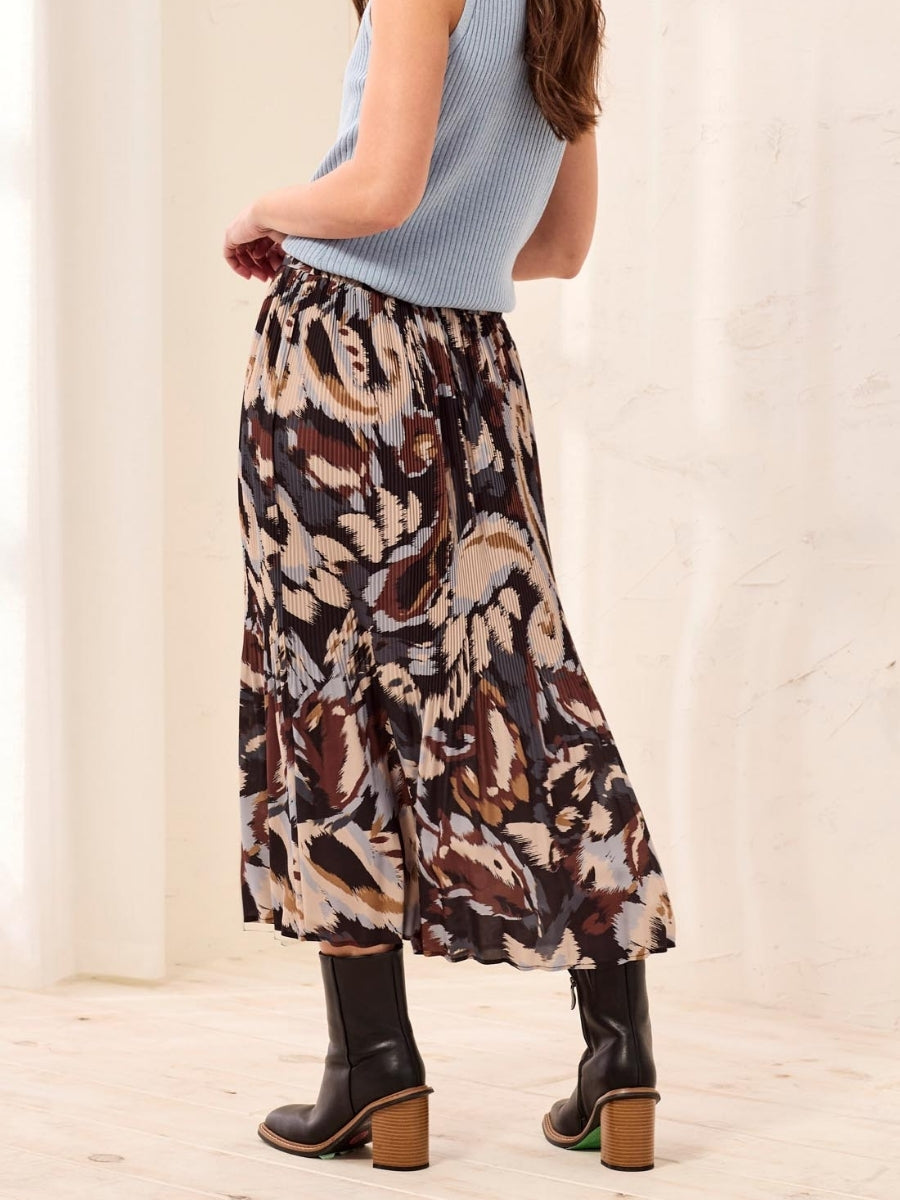Patterned pleated midi skirt paired with black heeled boots and a sleeveless blue ribbed top