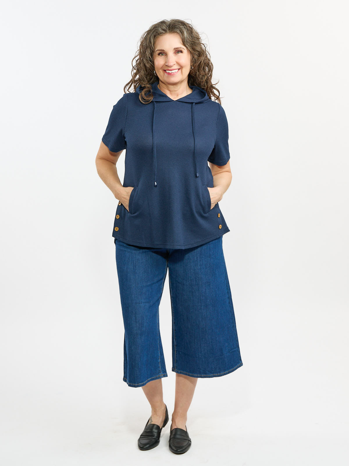 Navy short-sleeve hooded top with front pockets paired with wide-leg cropped denim pants and black slip-on shoes.