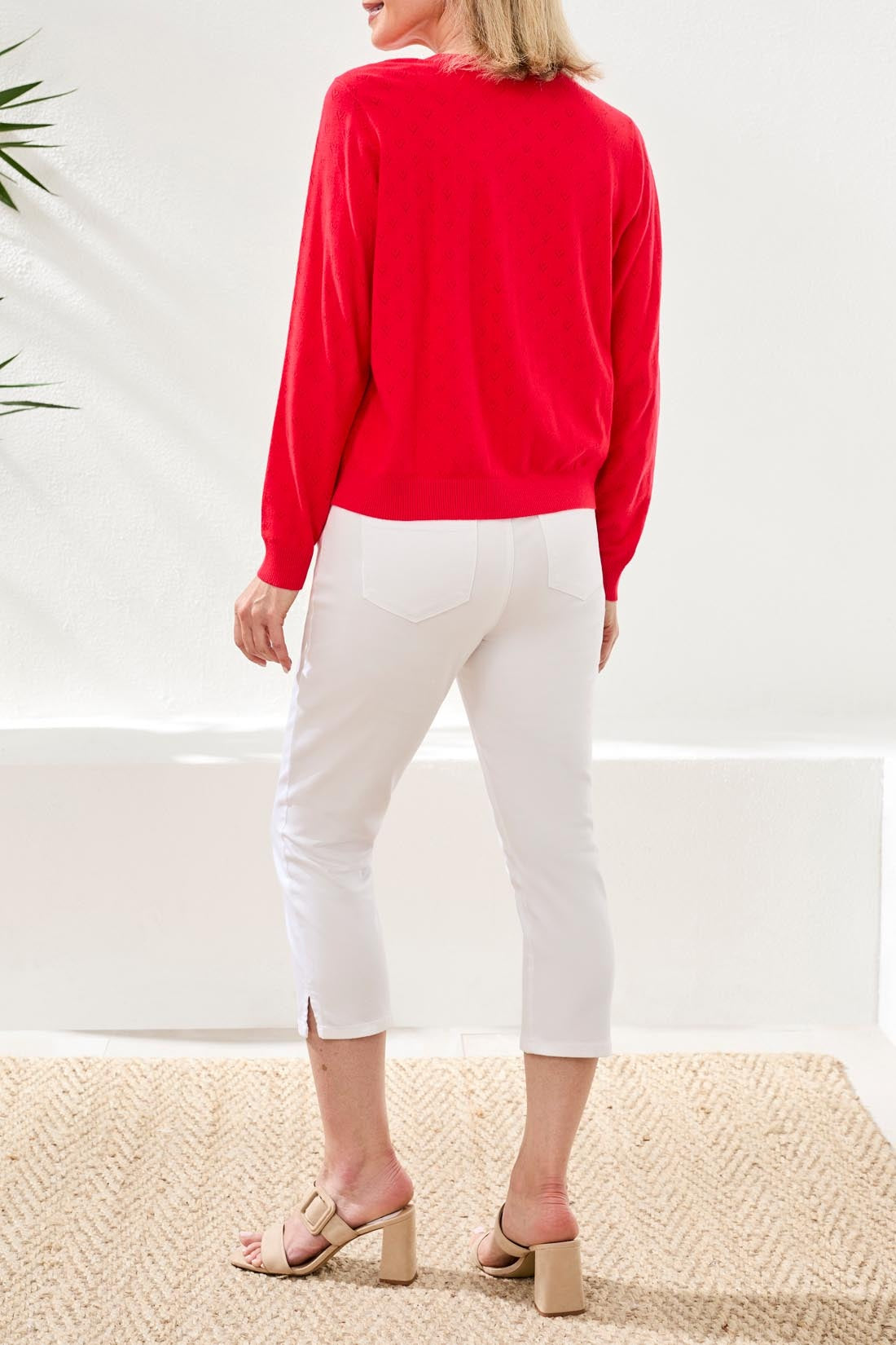 Back view of a red Tribal Playful Heart Pointelle Crew Cardigan by Tribal Sportswear Inc. paired with white pants and heels