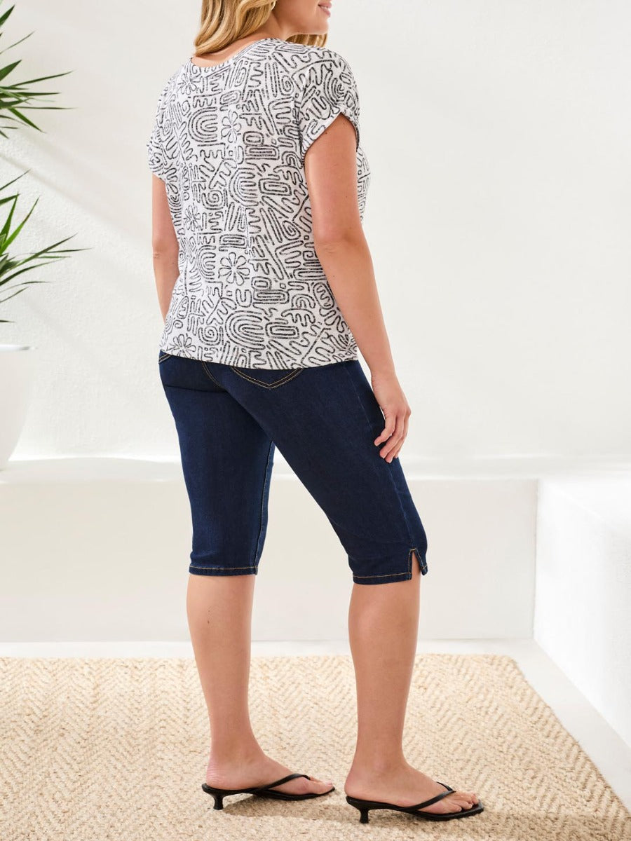 Tribal Wear-Me-Two-Ways Printed Short Sleeve Top by Tribal Sportswear Inc., white with black abstract print, paired with denim shorts.