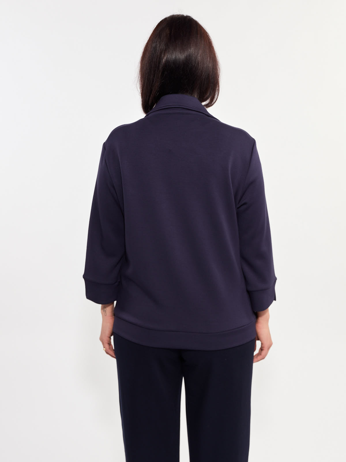 Back view of a navy blue long-sleeve jacket with a collar and ribbed cuffs, paired with dark pants.