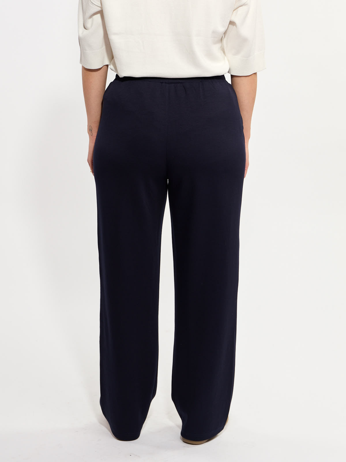 Back view of loose-fitting navy blue wide-leg trousers with an elastic waistband paired with a cream top