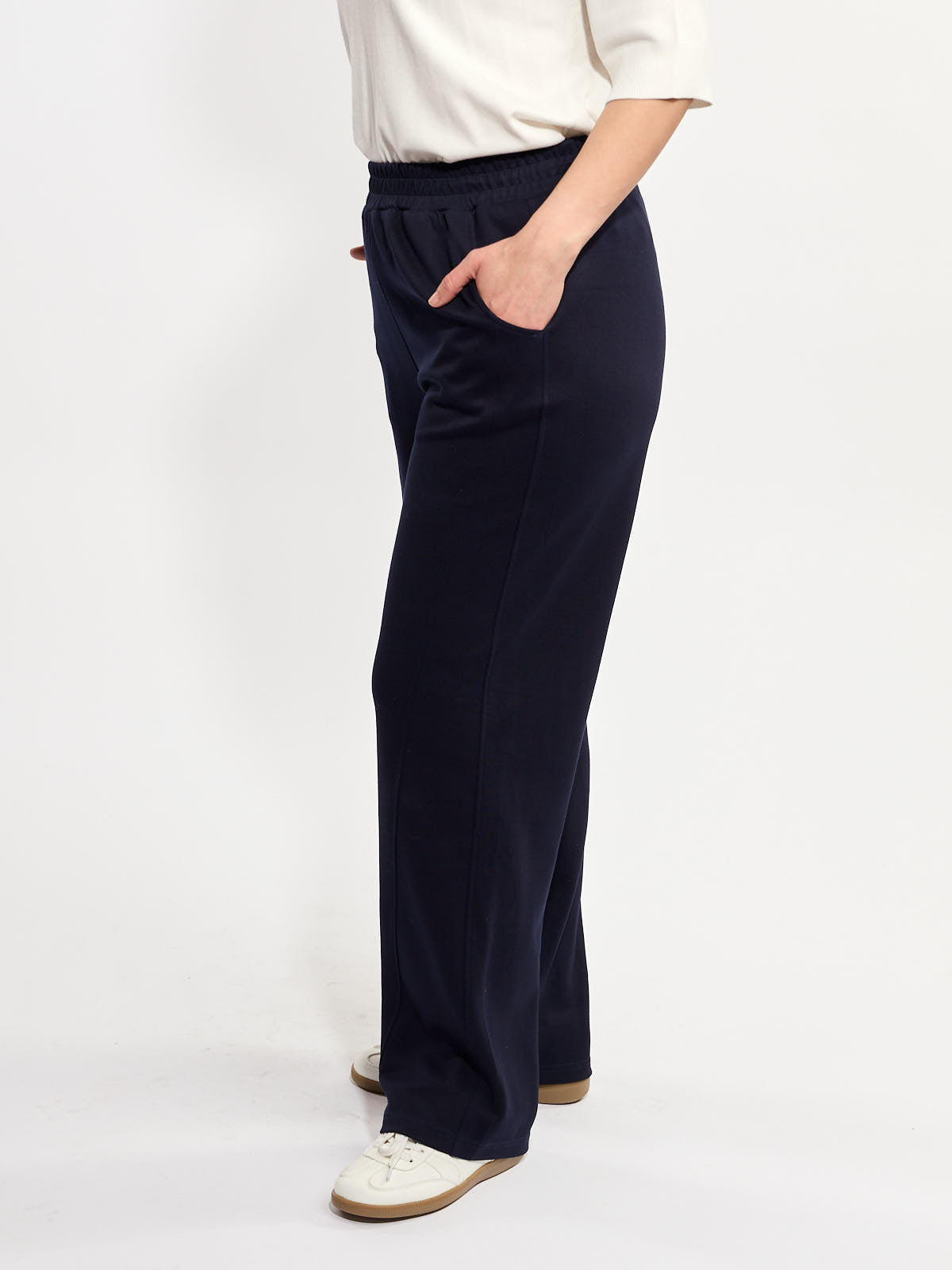 Navy blue wide-leg pants with elastic waistband and side pockets paired with white sneakers and light top.
