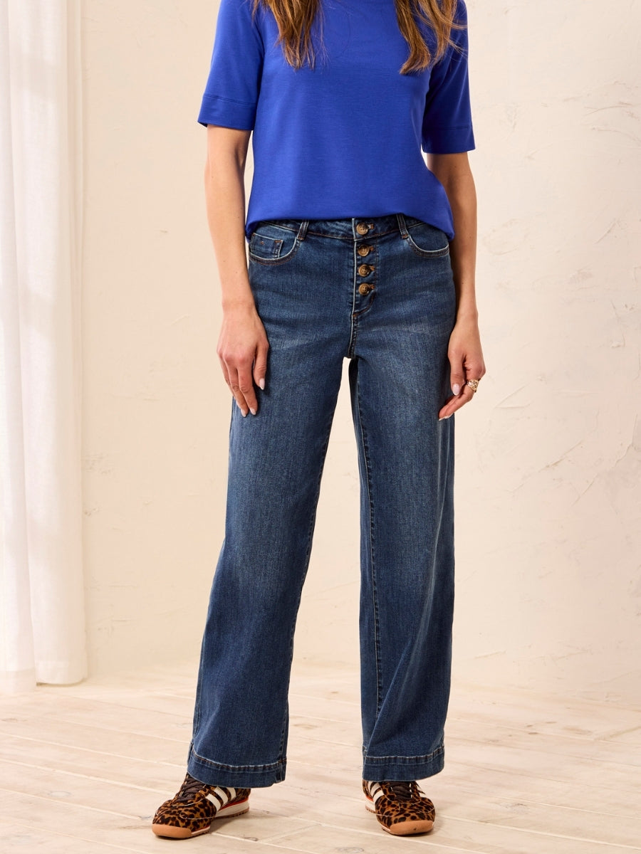 Straight-leg blue denim jeans with front button closure paired with a short-sleeve blue top and leopard print shoes.