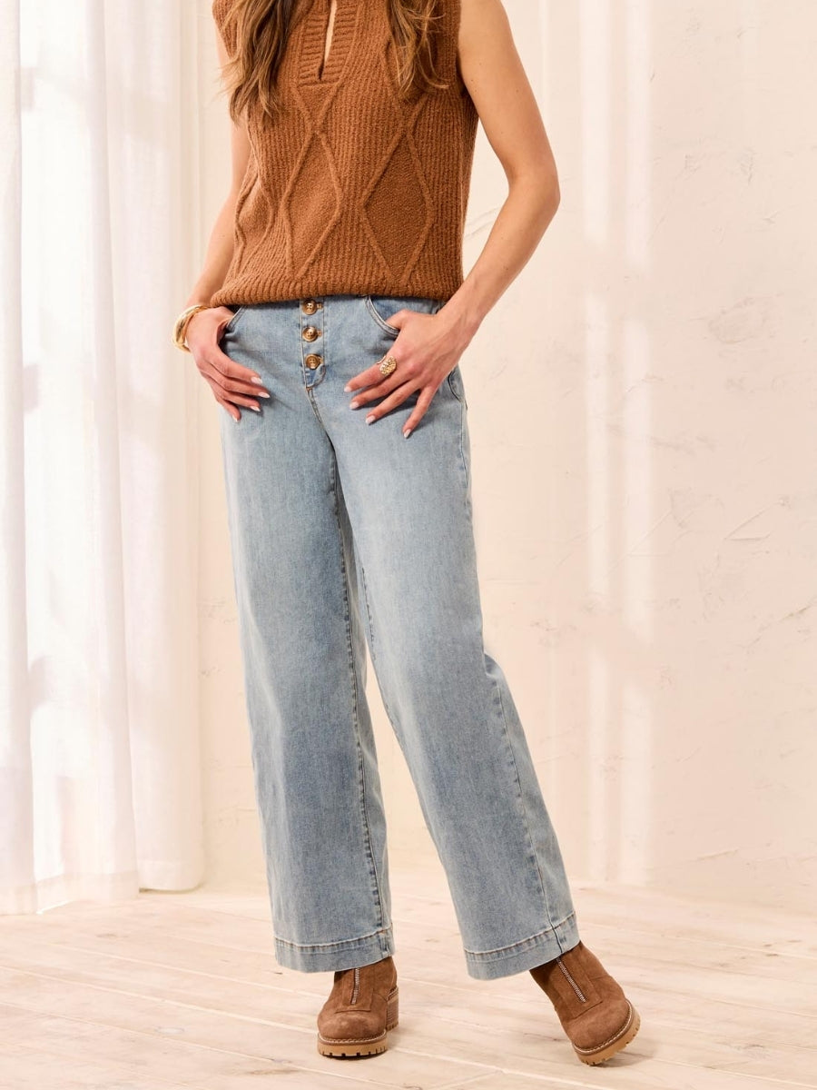Light blue wide-leg denim jeans with button fly paired with a textured brown sleeveless sweater and brown ankle boots.