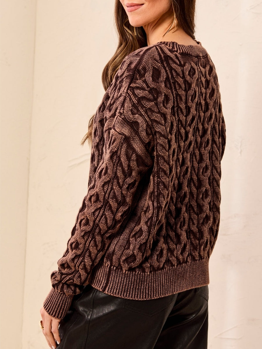 Brown cable knit sweater with ribbed cuffs and hem paired with black leather pants against a neutral background.