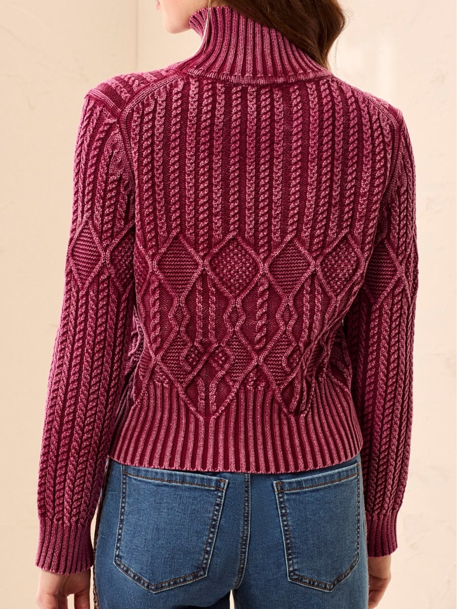 Back view of a burgundy cable-knit turtleneck sweater paired with blue denim jeans.