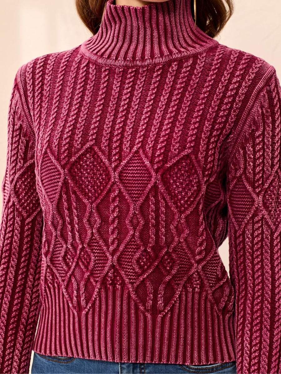 Burgundy cable knit turtleneck sweater with diamond and textured patterns across the front and sleeves.