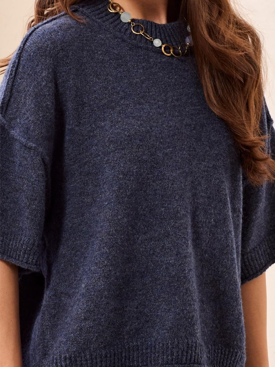 Close-up of a navy blue knitted sweater with short sleeves paired with a chain-link necklace featuring circular accents.