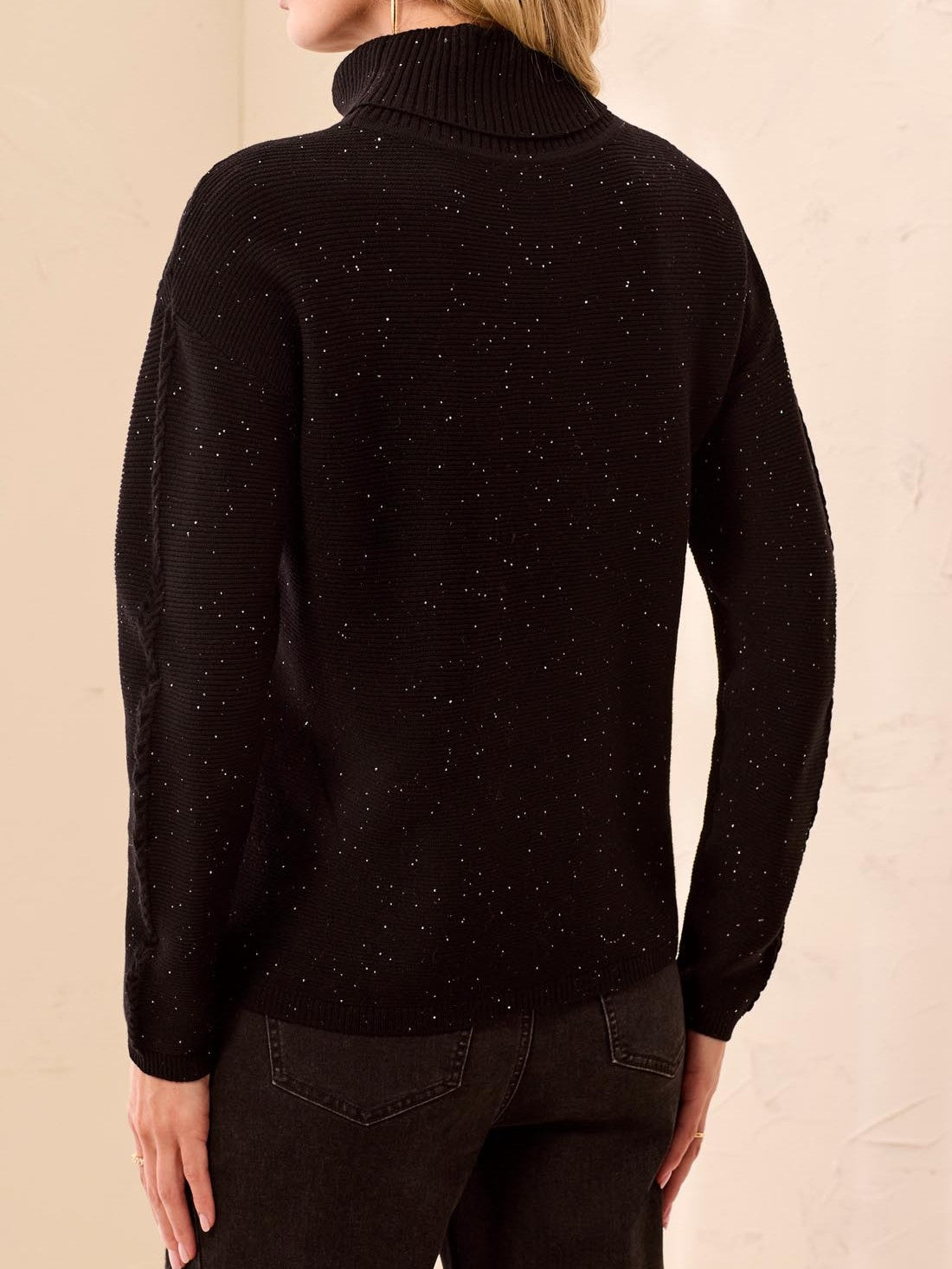 Back view of a black turtleneck sweater with subtle speckled texture and dark jeans