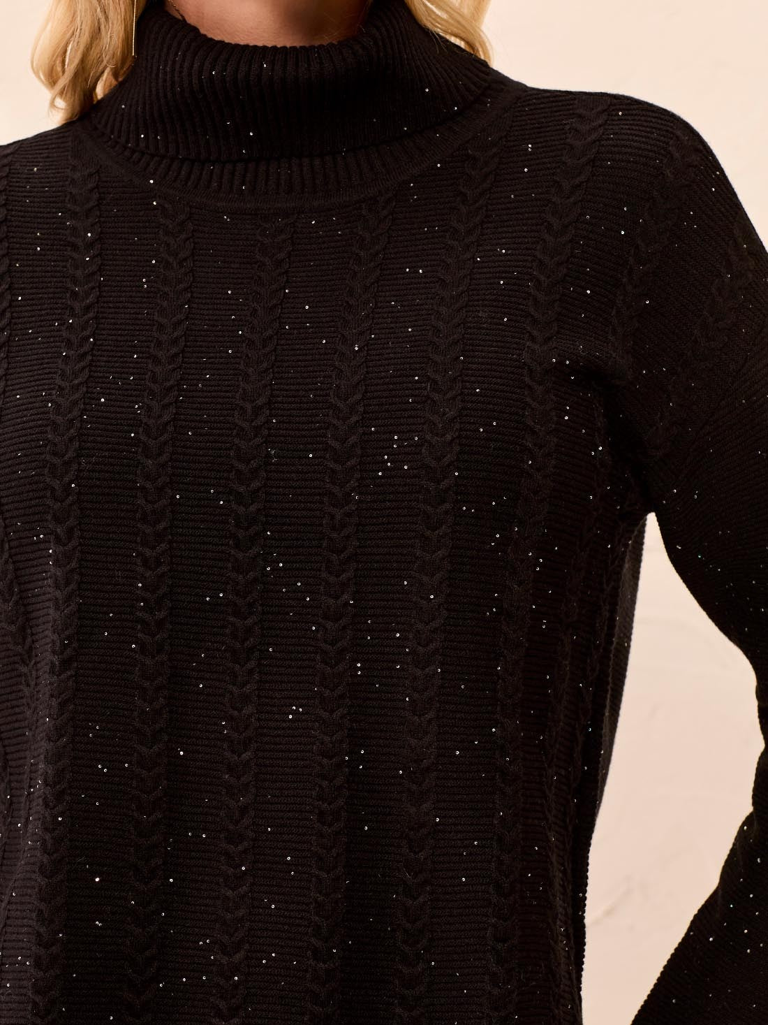 Black cable-knit turtleneck sweater with subtle flecks and long sleeves