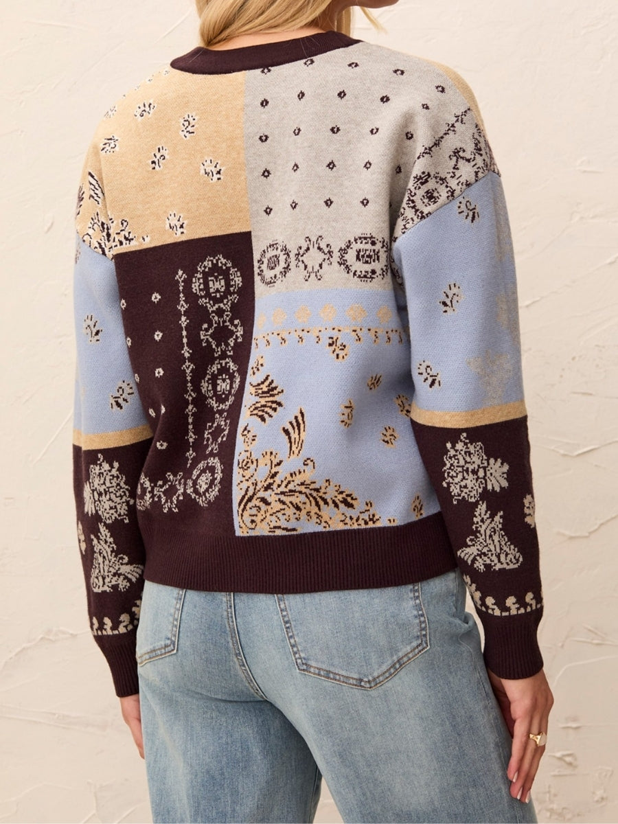 Knitted patchwork sweater with blue, beige, and brown sections featuring intricate floral and geometric patterns.