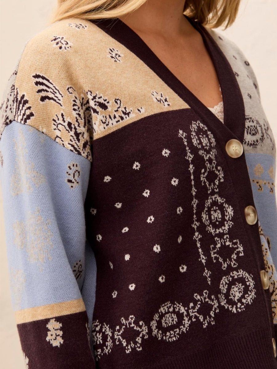 Close-up of a multicolored knitted cardigan with floral and geometric patterns and large beige buttons.