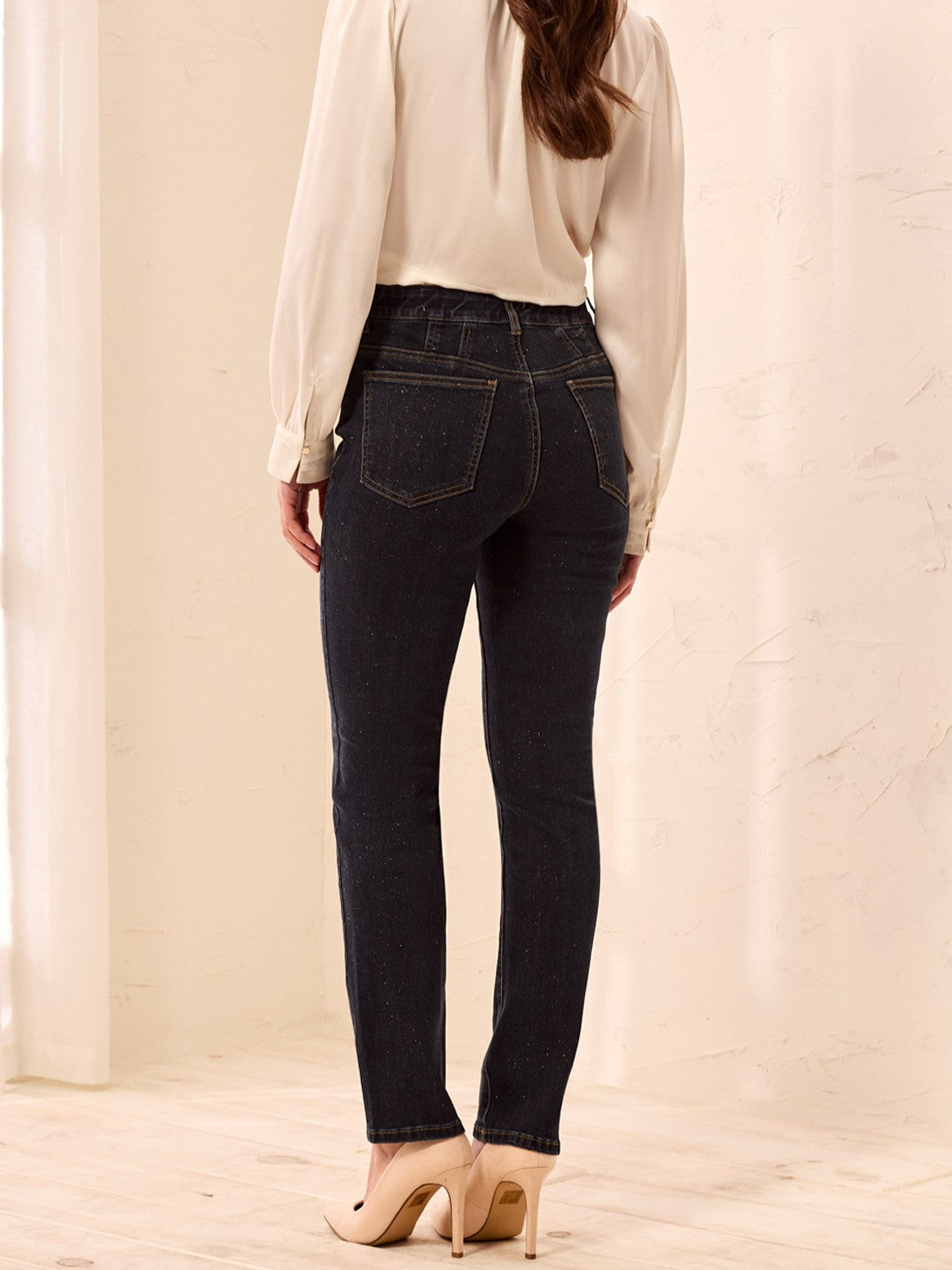 Rear view of a figure in dark denim jeans, cream blouse, and beige heeled sandals