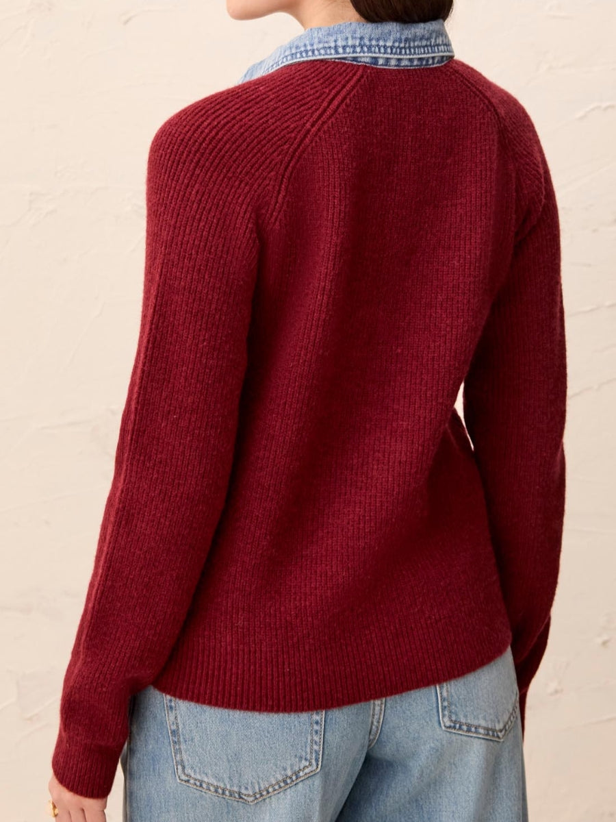 Dark red knit sweater with long sleeves layered over a light blue denim shirt, paired with light wash denim jeans.