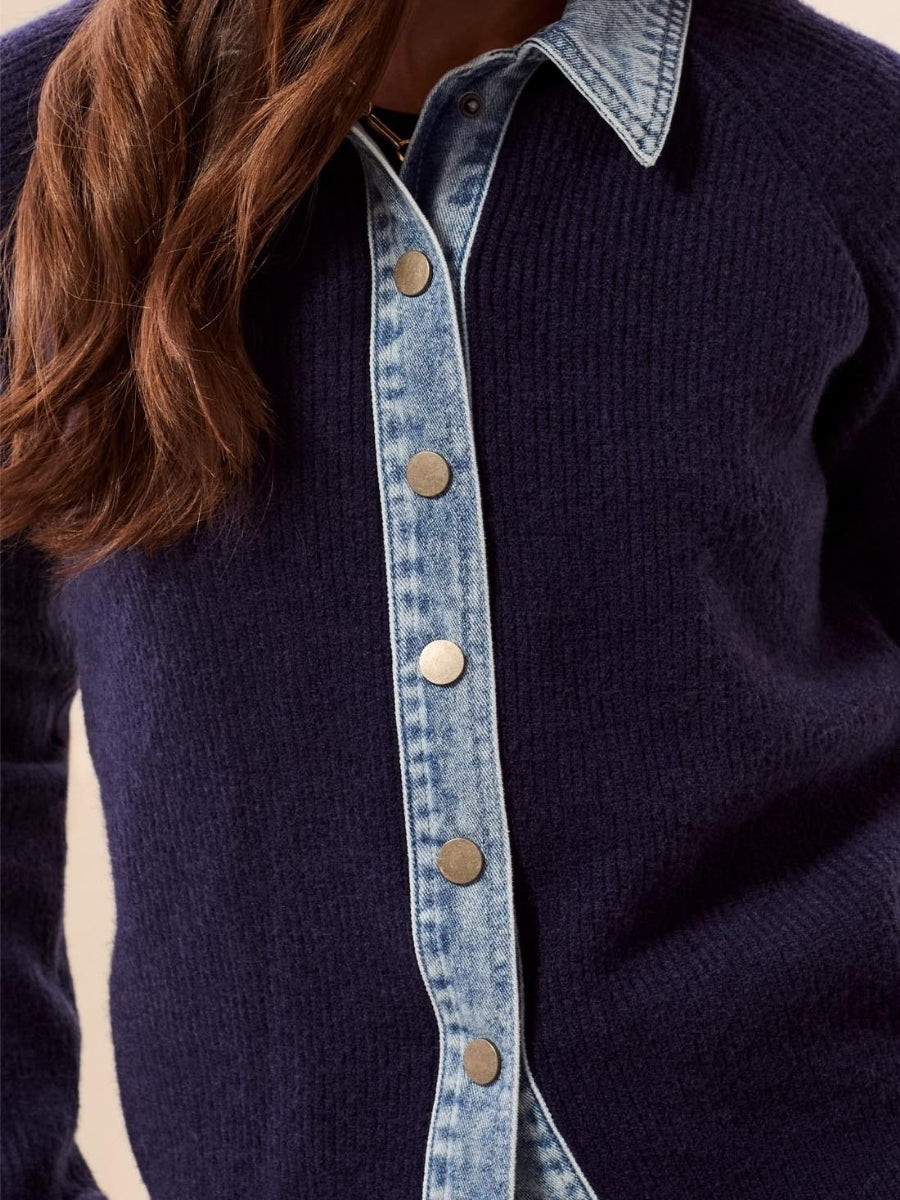Close-up of a navy knitted sweater layered over a light blue denim button-up shirt with metal snap buttons.