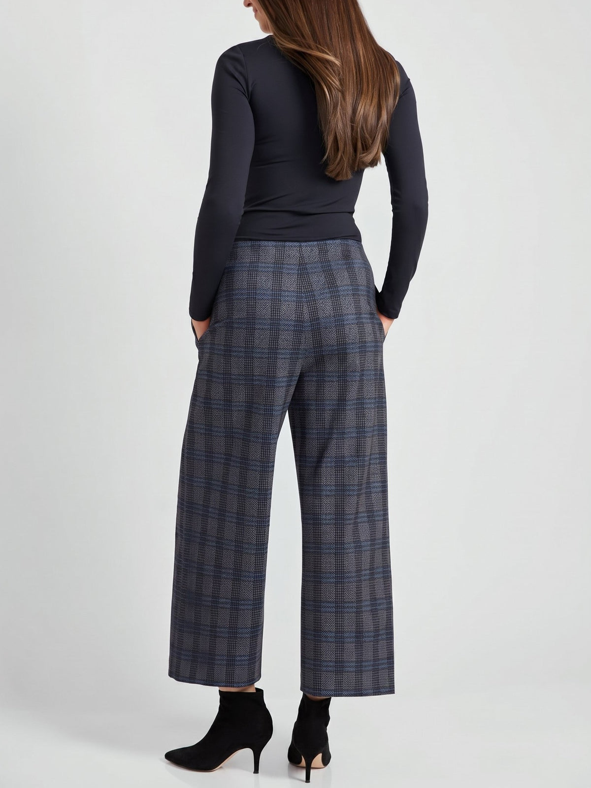 Back view of a figure in a black long-sleeve top and gray plaid wide-leg trousers with black heeled boots.