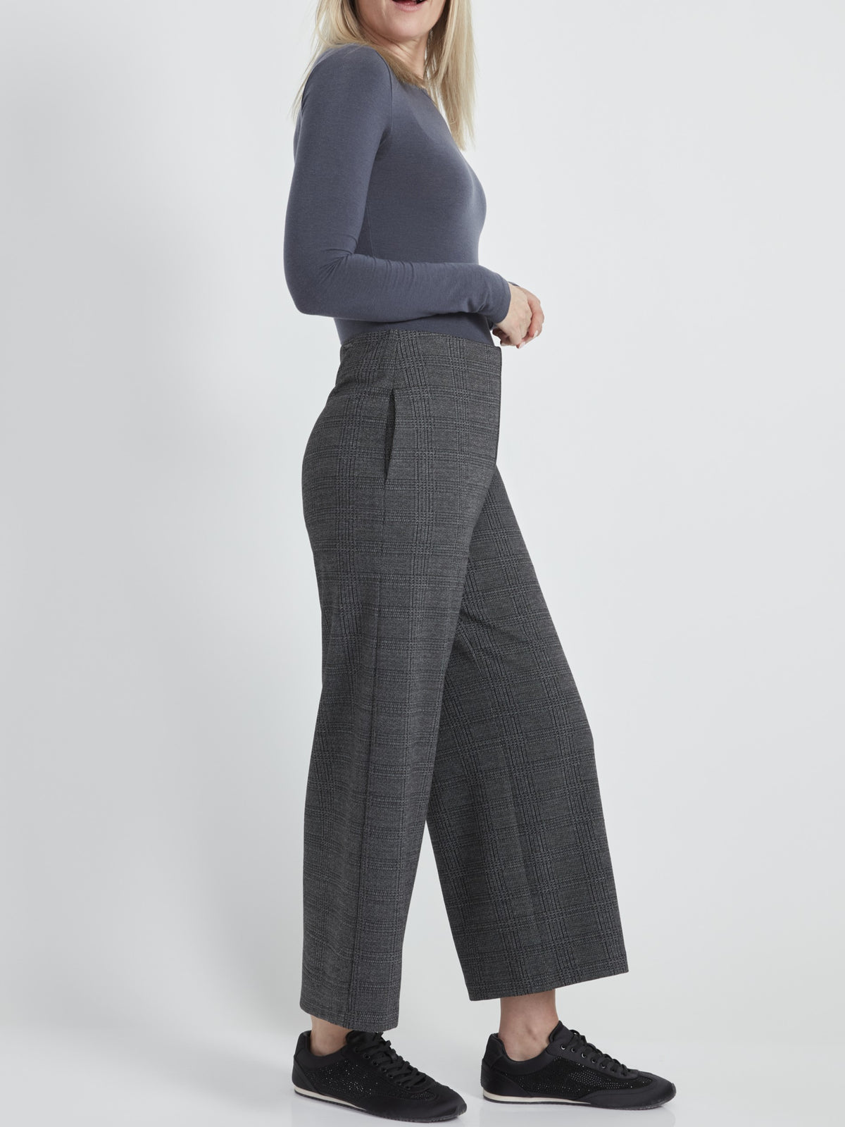 Side view of a figure in a fitted long-sleeve top and gray wide-leg checkered trousers with black sneakers