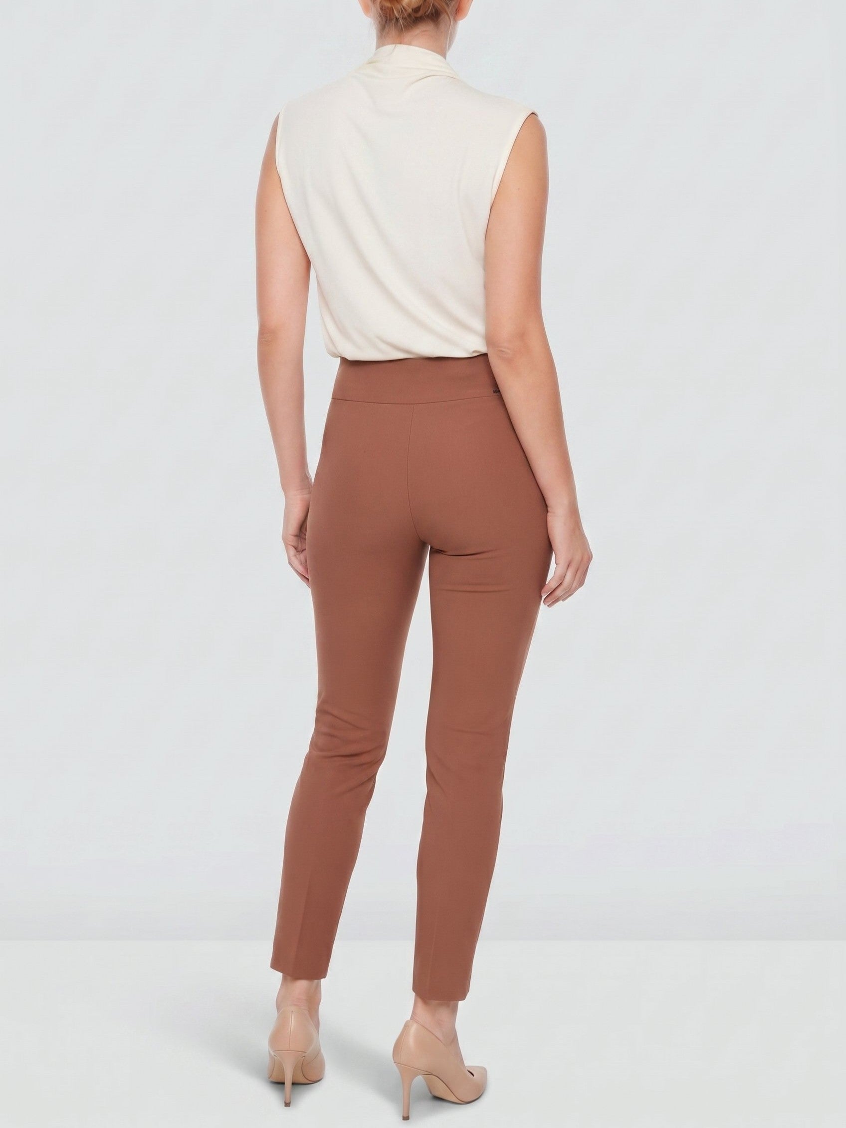 Back view of a figure in sleeveless beige top and fitted brown pants with nude high heels on a light background.