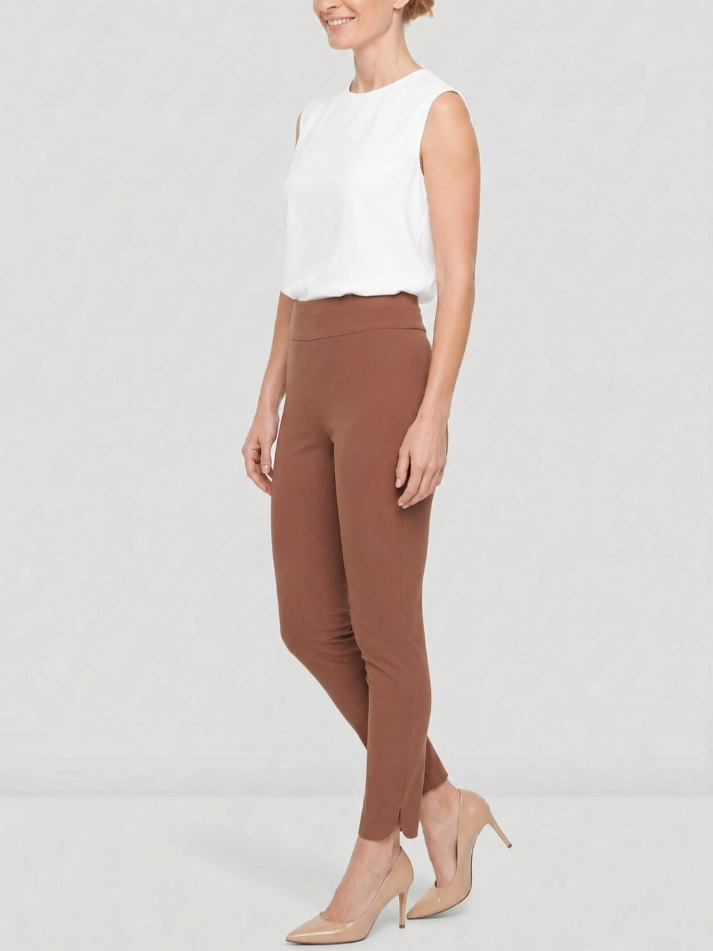 Slim-fit brown pants paired with a sleeveless white top and beige high-heeled shoes on a plain background.